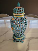 Front view of glazed pottery candle holder showing ornate cutout pattern and floral decoration.