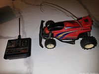 Photo of the red Nikko remote control car with black front bumper and large knobby tires, showing decals and antenna.