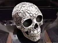 Front view of intricate floral carved resin skull figurine with detailed petals and leaves on surface.