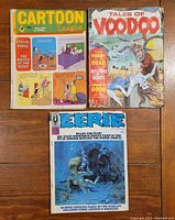 Photo of three vintage comic books on wooden surface: Cartoon Laughs, Tales of Voodoo, Eerie