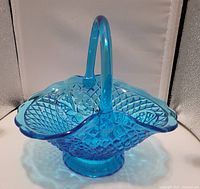 Blue glass basket with diamond point pattern and floral accents, shown at an angle highlighting handle and scalloped rim.