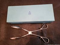 Photo of vintage silver plated serving tongs alongside the blue Birks box indicating original packaging and condition of the box.