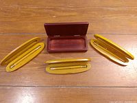 Three wooden pens each in individual curved wooden pen holders, arranged around a rectangular wooden box with hinged lid, set on a wood surface.