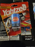 Photo of original blister pack containing the blue plastic Yahtzee cup, 5 dice, keychain clip, score pad, chips, and pencil, with visible folds in packaging.
