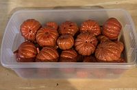 Plastic orange pumpkins stored in a rectangular plastic container showing multiple pumpkin shapes and sizes.