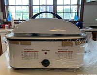 Front view of the white Betty Crocker roasting oven showing the closed lid with handle and protective plastic wrapping.