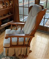 Side angle of the light blue upholstered wooden rocking chair highlighting the armrest and skirt detail