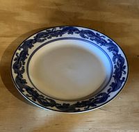 Oval ceramic plate with blue floral and scroll pattern on white background with gold trim, photographed on wooden surface