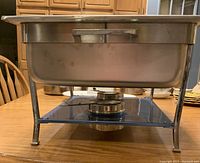 Side view of stainless steel chaffing dish on a stand with burner beneath.