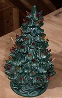 Full view of green ceramic Christmas tree with multicolored bulbs resembling Christmas lights attached on tips of branches.