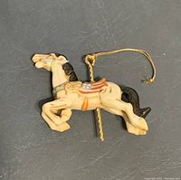Close-up of a single Christmas ornament: a cream-colored winged horse with black mane and tail, decorated with an American flag saddle and attached gold string for hanging.