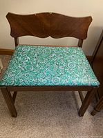 Green wooden bench with floral upholstery and wooden backrest.