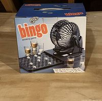 Boxed bingo drinking game showing cage for numbered balls, game tray, cards, and glasses
