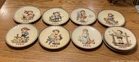 Ten unboxed Hummel standard size collector plates arranged on table showing various years and scenes
