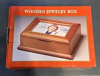 Image of a rectangular wooden jewelry box in original packaging, featuring a photo frame on the lid.