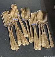 Photo shows a cluster of silverware forks with ornate floral patterned handles, approximately 18 forks.