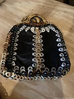 Black purse with tan and black woven leather trim and circular handle on wooden floor