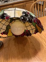 Close-up of the light fixture showing the round white bulb inside the stained glass shade with grape clusters, pears, and berries.