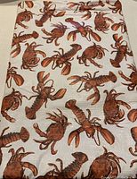 Photo of lobster patterned vinyl tablecloth showing multiple lobsters in brown-red print on cream background.