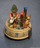 Wooden music box with boy playing violin, birds and cat figurines on circular base with floral and tree pattern