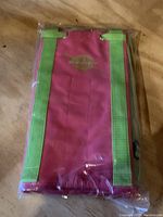 Top view of one folded Nantucket Bagg tool bag in pink with green straps and logo visible inside original packaging.