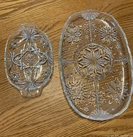 Two clear glass platters with star and floral pressed glass designs on wooden surface, one elongated oval and one divided section platter.