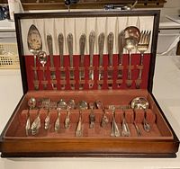 Full view of two sets of silver plated silverware arranged in a wooden case with fabric lining