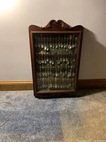 Full view of wooden glass display case with decorative top, showing hanging rows of spoons inside.