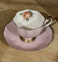 Close-up of porcelain teacup with pink exterior, rose floral interior design, and matching pink saucer with gold rim.