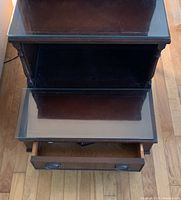 Top down view of the 3-tier wooden end table showing the glass top, two shelves, and open drawer with metal handles.