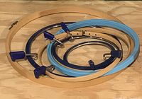Wooden and plastic embroidery hoops stacked together on a wooden surface, showing blue and purple clamp locks