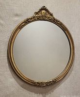 Front view of the round ornate mirror showing decorative gold-tone frame and clear mirror surface with minor age marks.