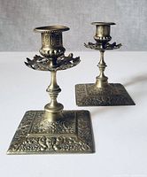 Front angled view showing both ornate brass candle holders with detailed embossed patterns and square bases.