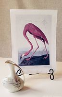 Photo showing the vase with floral design and gold leaf handle beside the flamingo print on an easel.