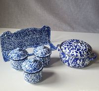 Photo of three blue and white speckled enamelware containers with lids, their matching pot with lid, and the wall hanger on a white surface.