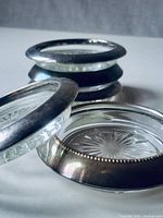 Set of six round glass coasters stacked with one coaster leaned on the side showing silver plated rim and starburst etched glass pattern.