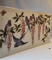 Full front view of the needlepoint textile showing birds on branches with flowers, mounted on wood frame.