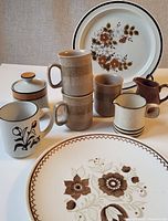 Photo showing all ceramics in the lot including mugs, plates, sugar bowl, and creamers arranged on table