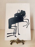Full view of the silkscreen print on a small easel showing the abstract spider-like figures.