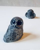Photo showing one owl carving in foreground with black eyes and detailed feathers, with the second blurred in background.