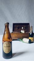 Close-up image of a vintage Guinness Extra Stout bottle with paper label and crown cap in front of a wooden box and other bottles in the background.