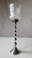 Front view of tall silver candleholder with frosted glass shade showing geometric etched pattern, wavy tiered stem, and round base.