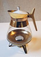 Full assembled coffee pot on metal burner with ceramic lid attached, showing gold lines and metal accents.