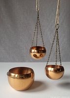 Three vintage Coppercraft Guild copper planters displayed with two small hanging planters suspended by chains and one larger handled planter placed upright.