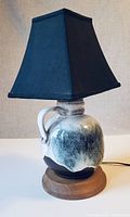 Front and side view of the vintage ceramic lamp with blue fabric shade sitting on wooden base, showing glaze details and handle on ceramic body.