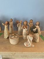 Seven carved wooden Willow Tree angel figures and oval trinket box arranged on a surface, showing full set and overall look.