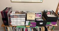 Stack of various art magazines and boxes with photo cards on a wooden table.
