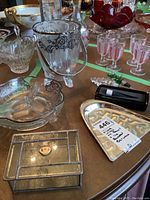 Overview of footed ice bucket, etched bowls, rectangular glass trinket box, silver-tone ashtray, and pink glass goblets on table.