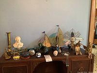 Full view of all items on wooden furniture including stained glass pieces, Blue Mountain figurines, brass candlestick, miniature bust, paperweights, decorative figurines.