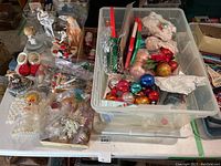 Overview of Christmas-themed items on table with large plastic tote containing ornaments, tinsel, and other decorations.